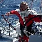 Nodas at the helm in a red sailing jacket, in a strong breeze.