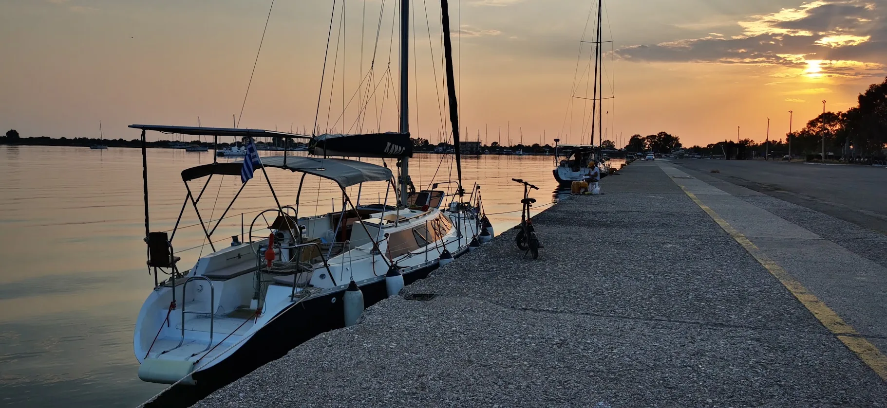 Water Mellon moored alongside the Messolonghi town quay at sunset, with a folding bicycle on the quay and calm water.