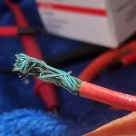 Close-up of an old red cable from Water Mellon, its copper strands green with corrosion.