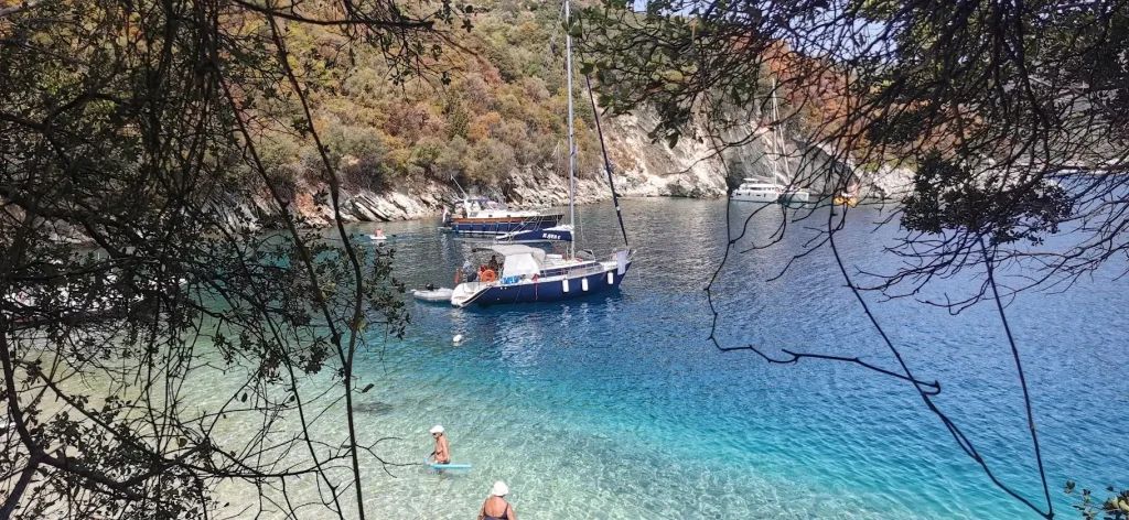 Water Mellon at anchor in a turquoise bay on Lefkada, seen through the trees from the shore.
